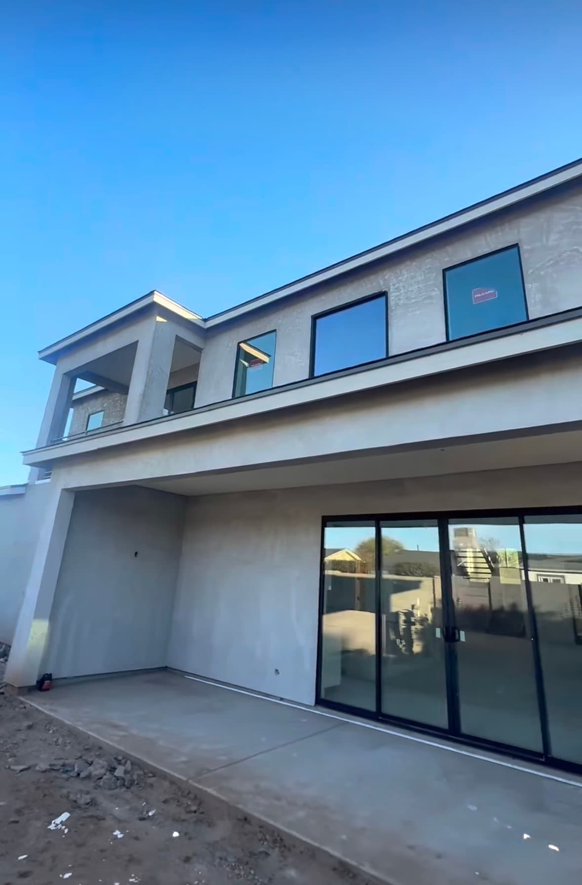New modern gray stucco house with large windows and a concrete patio under blue sky.