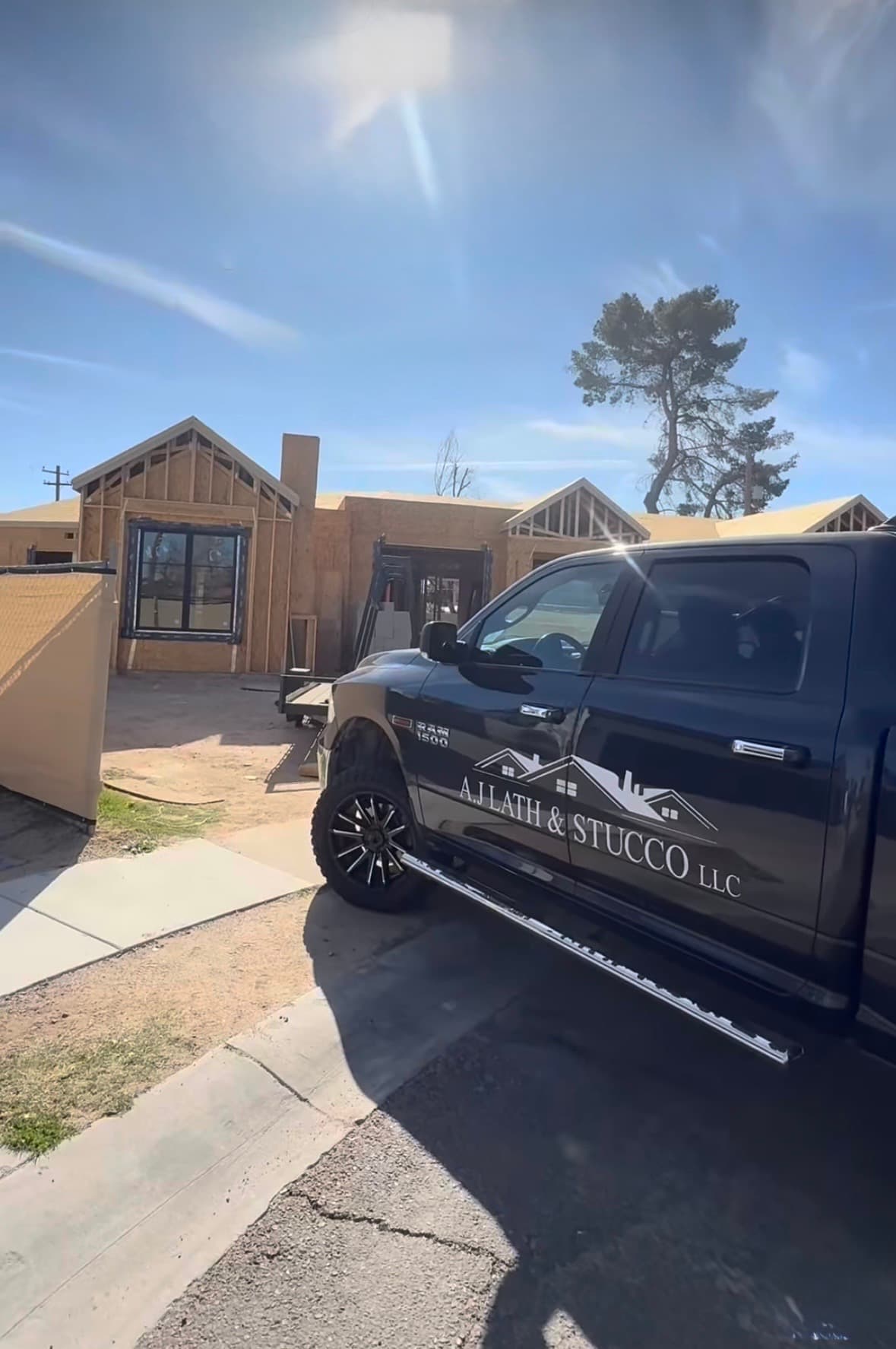 Black "A.J. LATH & STUCCO" truck parked at a framed house under construction on a sunny day.
