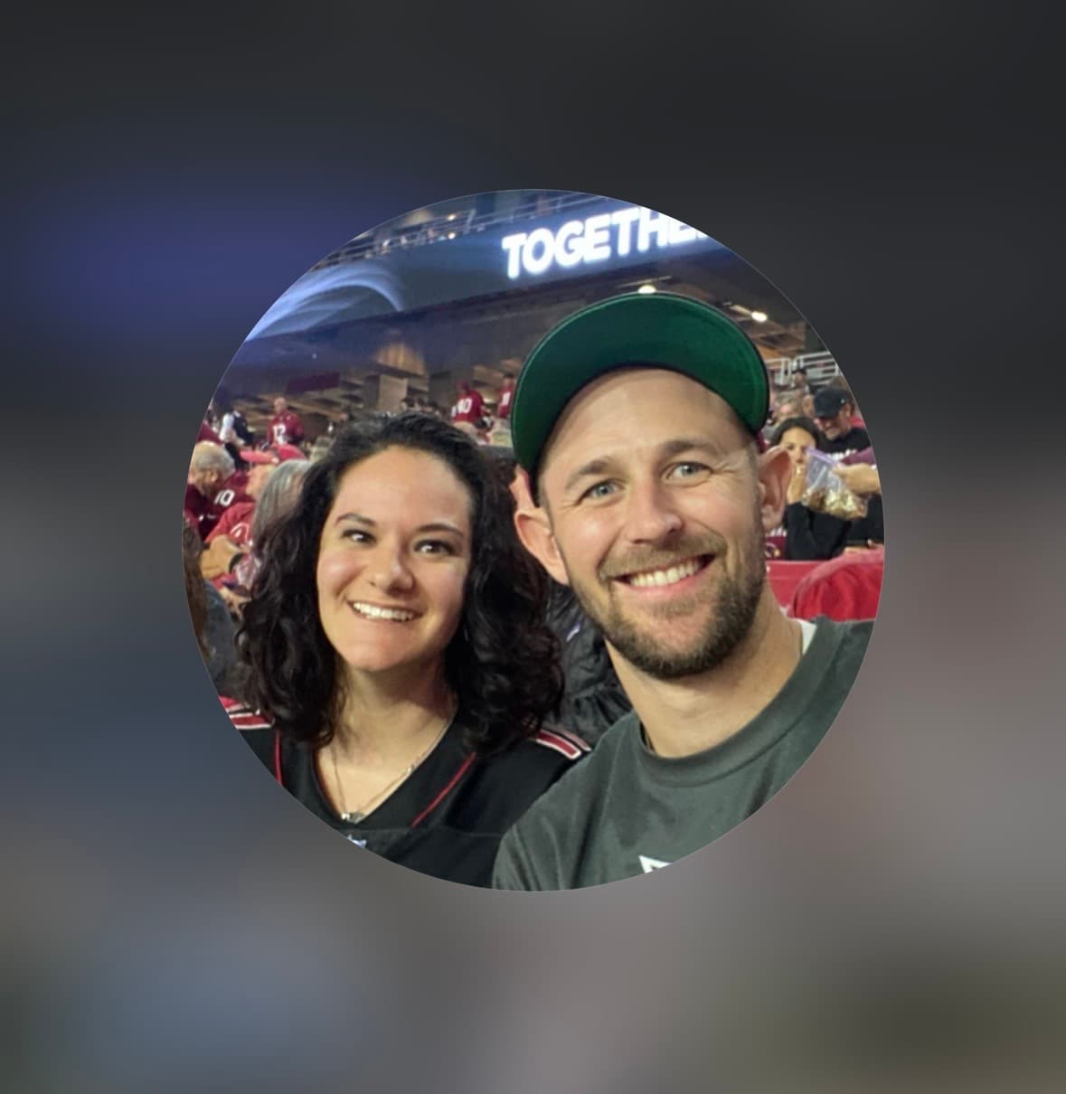 Smiling man in a green cap and woman with dark curly hair at a stadium.