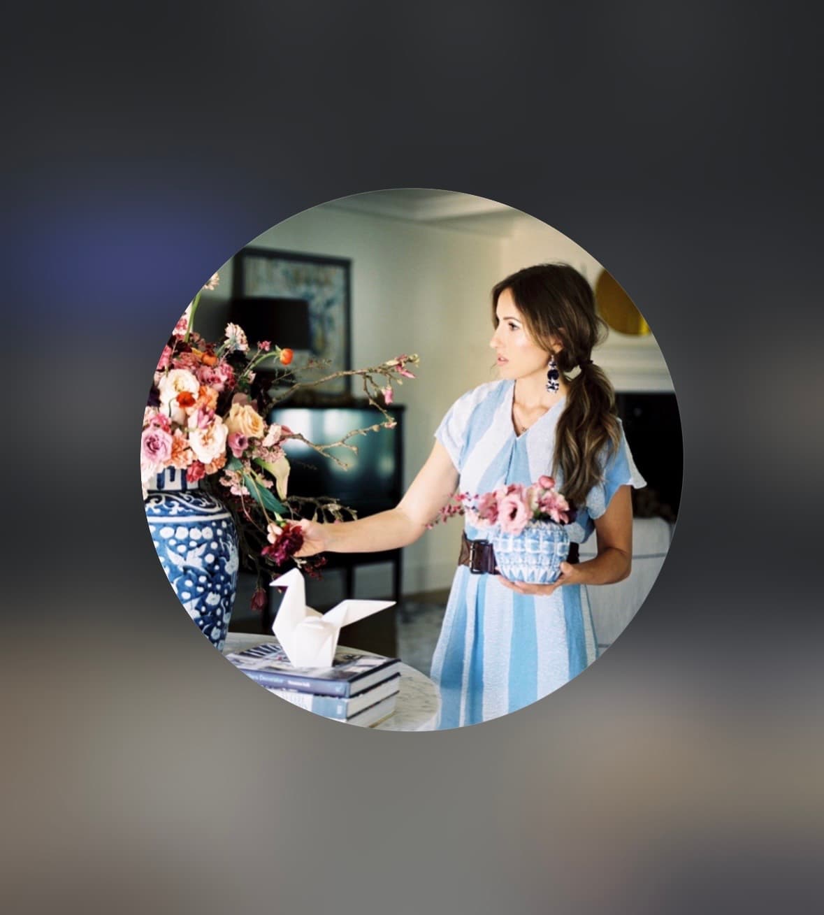 Woman in a blue striped dress arranging pink flowers in blue and white ceramic vases.