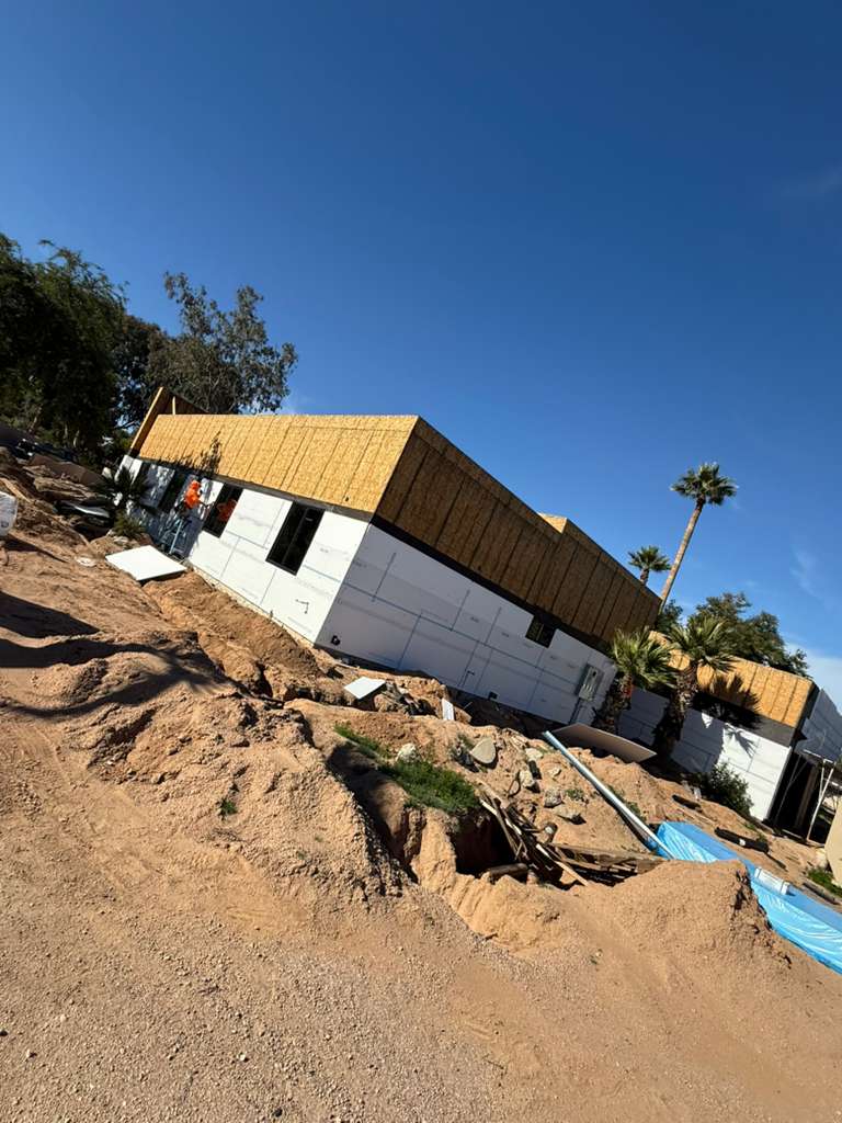 House under construction on a desert hillside, with palm trees and clear blue sky.