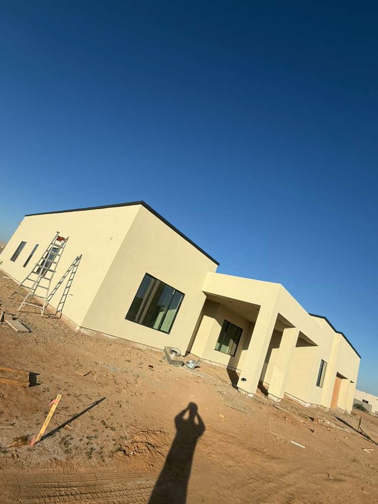 Modern light-colored house under construction in desert landscape with clear blue sky.